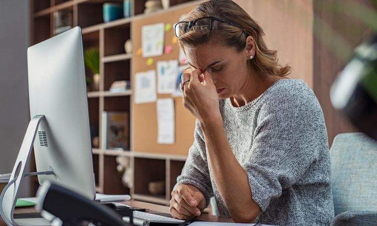 woman at desk fingers on bridge of nose 768